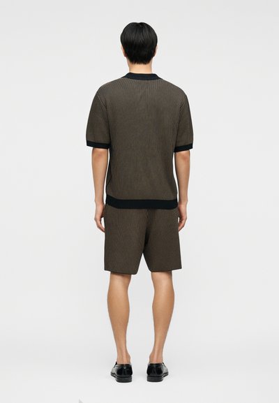 Homme debout de dos, portant une chemise à manches courtes rayée verticalement marron et noire ainsi que son short assorti, avec des chaussures habillées noires.