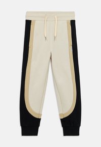 Φόρμες σε μπεζ και μαύρο μείγμα βαμβακιού, με μεγάλες καμπυλωτές πλευρικές φάσες σε λείο υλικό, με ελαστική μέση με κορδόνι και ριμπ μανσέτες.