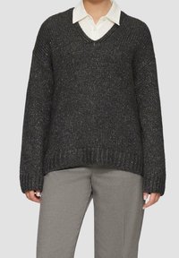 Mørkegrå strikket sweater med v-hals, oversized pasform, sænkede skuldre og tekstureret stof med subtile metallic tråde. Kombineret med grå bukser.