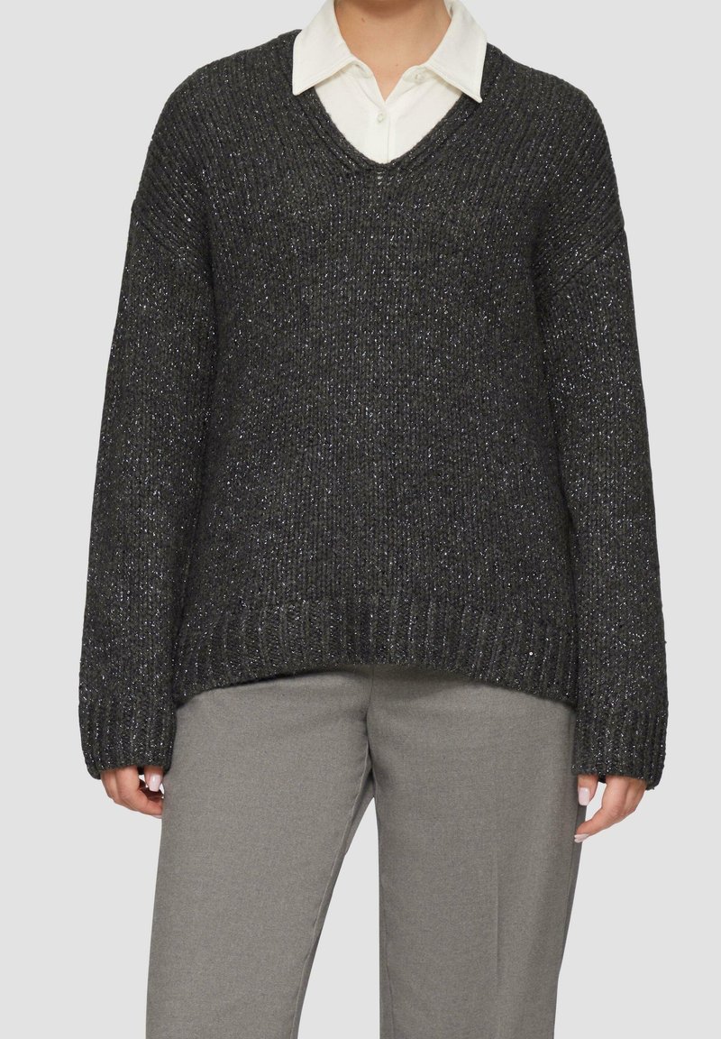 Mørkegrå strikket sweater med v-hals, oversized pasform, sænkede skuldre og tekstureret stof med subtile metallic tråde. Kombineret med grå bukser.
