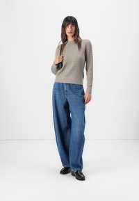 Lichtgrijze gebreide sweater met een gestructureerd patroon, gecombineerd met losse blauwe denim jeans en zwarte schoenen. De outfit heeft een casual, ontspannen pasvorm.