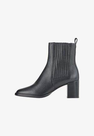 Bottine en cuir noir avec un bout pointu, des panneaux latéraux côtelés et un talon épais. Texture lisse avec un design épuré et fermeture éclair.