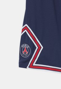 Granatowa koszulka sportowa z czerwonym i białym wykończeniem. Posiada okrągłą naszywkę z logo Paris Saint-Germain w dolnym lewym rogu. Miękka tekstura materiału.