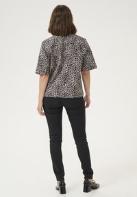 Chemisette à manches courtes en imprimé léopard beige et noir, associée à un jean skinny noir et des chaussures à talons, vue de dos.