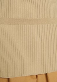 Beige ribbad stickad tyg med en jämn textur. Har vertikala ränder och en åtsittande design. Sömmen är rak och snyggt avslutad.