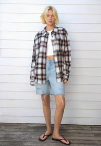 Geruite button-up shirt in wit, rood en marineblauw; gecombineerd met lichtblauwe, verwassen denim shorts en bruine teenslippers. Zachte textuur.