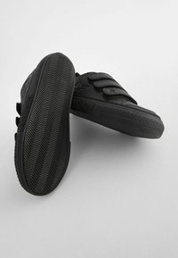 Baskets noires avec une empeigne synthétique lisse, trois bandes Velcro, semelles en caoutchouc texturé avec un motif en chevrons, et un branding Pokémon.