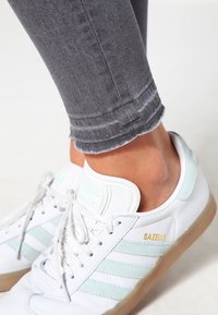 Zapatillas de cuero blancas con rayas y acentos en verde menta, que cuentan con una suela de goma y jeans de mezclilla gris deshilachados de longitud hasta el tobillo.
