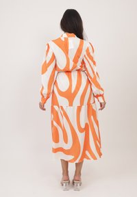Vestito a maniche lunghe caratterizzato da un motivo ondulato arancione e bianco, realizzato in un tessuto morbido, con vita arricciata e design a strati della gonna.