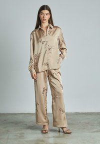 Set di pigiama in satin beige chiaro con ricami floreali. Comprende una camicia con bottoni e pantaloni a gamba larga. Accentuato da sandali con tacco alto.