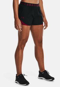 Černé sportovní šortky s mahagonovým vnitřkem, s širokým pásem s nápisem "UNDER ARMOUR" tučným písmem.