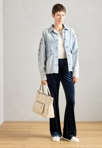 Denim jaka ar gaiši zilu tonējumu un nolietotu apakšmalu, kombinēta ar tumši zilo samta platā kāju biksēm un baltām slip-on kurpēm. Beigmēta rokassoma ar akcentiem.