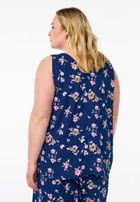 Top senza maniche a fiori con sfondo blu navy, caratterizzato da fiori rosa e verdi. Tessuto morbido, vestibilità comoda e dettaglio della fessura sul retro.
