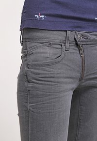 Grå denimjeans med smal passform, med dragkedja i gylfen, framfickor och en liten logodetalj på midjebandet. Byxorna har en slät textur.