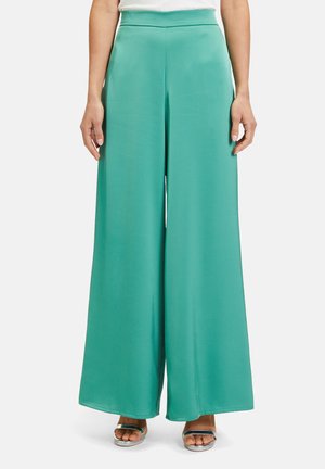 Pantalons à jambes larges en teinte sardonique, fabriqués à partir d'un tissu lisse. Dotés d'une taille haute et d'un ourlet uniforme. Associés à des sandales argentées.