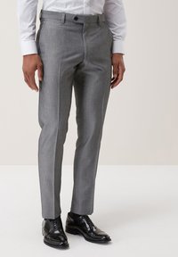 Grau maßgeschneiderte Hose aus glattem Stoff mit geradem Schnitt, seitlichen Taschen und einem Knopfverschluss. Schwarze Anzugschuhe runden den Look ab.