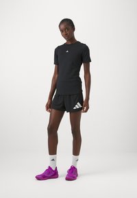 Mustvalge spordisärk ja lühikesed püksid, millel on valge Adidas'i logo, koos erksa lillaka kingadega. Särgil on lühikesed varrukad; püksid on vabad ja mugavad.