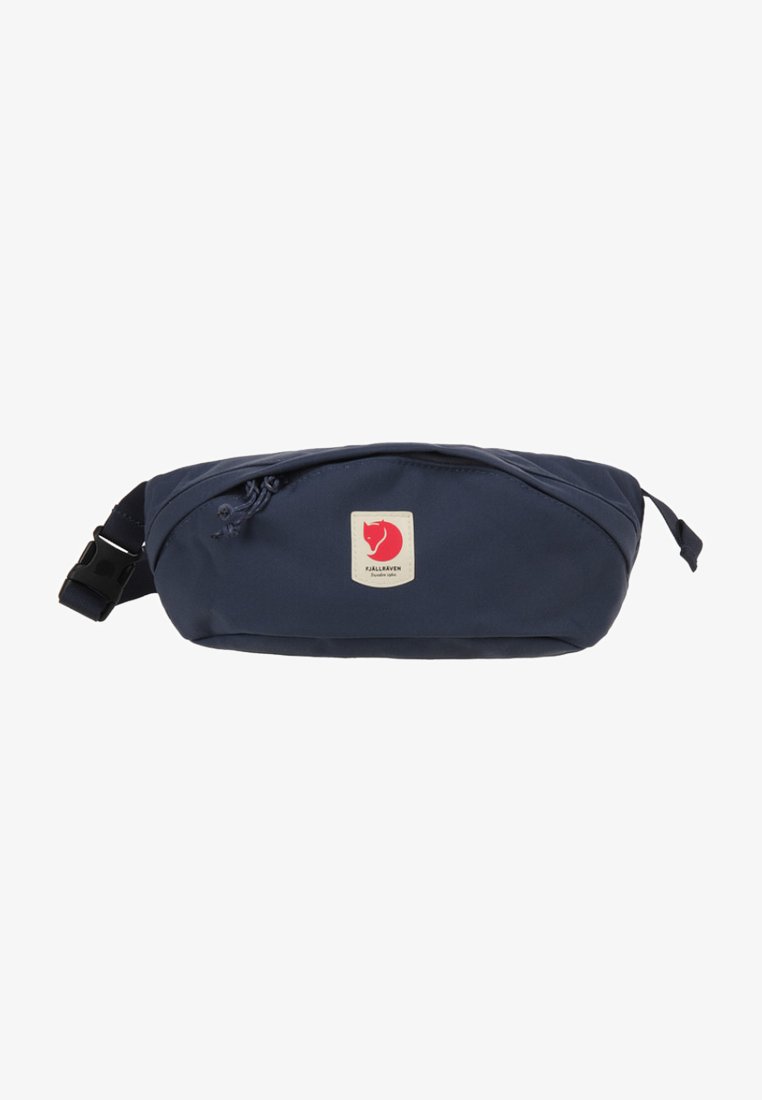 Marsupio in tessuto blu navy con forma curva, tasca frontale con zip e un'etichetta rossa con un simbolo di una volpe stilizzata. Cinghia regolabile.