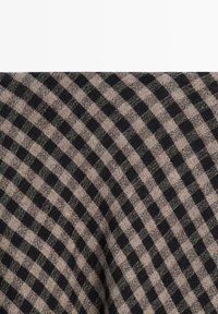 Gros plan d'un tissu avec un motif à carreaux diagonaux noirs et beiges et une texture tissée visible.