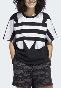 Svartvit randig oversized t-shirt med en distinkt geometrisk design, ihop med svarta shorts som har ett repetitivt logomönster.