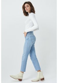 Jeans de tiro alto en azul claro con pierna recta, combinados con una blusa ajustada de manga larga blanca y botas de tobillo crema. Diseño simple, sin patrones.