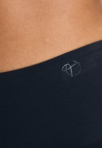 Black fabric waistband, smooth texture, with a subtle logo detail. The image focuses on the waistband area against skin tone.