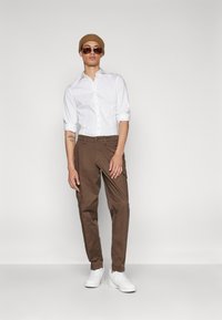 White button-up shirt, brown cargo pants, white sneakers, and a brown beanie; sunglasses complete the casual outfit.