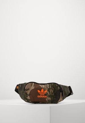 Banane Adidas à motif camouflage avec logo orange et sangle noire réglable posée sur une surface géométrique blanche.