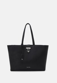 Černá taška přes rameno vyrobená z texturované kůže, s dvěma uchy, stříbrnými doplňky a předním zapínáním. Logo je vytištěno na spodní části přední strany.