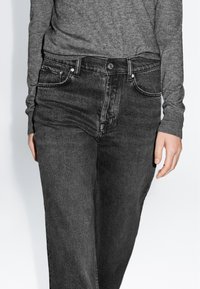 Jeans in denim nero con taglio dritto, caratterizzati da un classico design a 5 tasche, cuciture visibili e chiusura con bottone frontale.