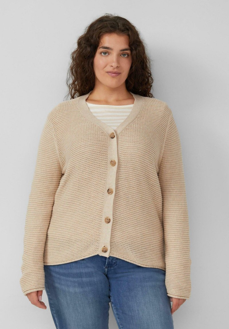 Beige, gebreide cardigan met een V-hals, lange mouwen en vijf houten knopen aan de voorkant. Guti over een wit gestreept shirt.