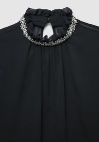 Schwarze Bluse mit gerafftem Rundhalsausschnitt, verziert mit klaren, funkelnden Verzierungen. Glatte Textur mit plissierten Details.