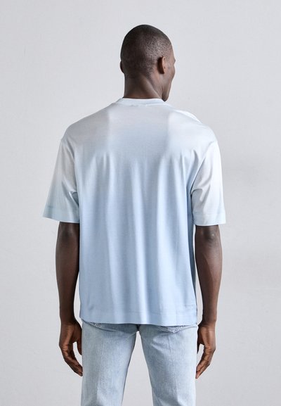 Ανοιχτό γαλάζιο κοντομάνικο μπλουζάκι με λεία υφή, ελαφρώς πιο σκούρες μανίκες, στρογγυλή λαιμόκοψη και άνετη εφαρμογή, φορεμένο με ανοιχτό τζιν.