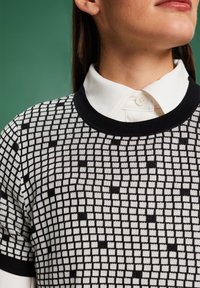 Top de punto a rayas en blanco y negro con cuello redondo, que presenta un diseño de cuadrícula y un cuello de camisa blanca superpuesto.