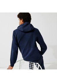 Sweatshirt navy avec capuche, présentant un panneau inférieur texturé et des poignets côtelés. Tissu lisse avec une coupe décontractée.