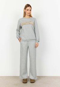 Szürke kapucnis pulóver "Amazing" felirattal arany színben, amelyhez illeszkedő, bőszárú szürke nadrág tartozik. Az anyag lágy és kényelmesnek tűnik.