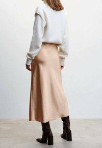 Long beige satin skirt paired with a white, fluffy knit sweater. Brown high-heeled boots complete the outfit. Rear view, minimalist background.