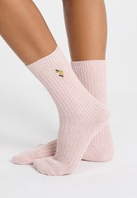 Piernas que llevan calcetines de caña corta de rayas rosa con una pequeña flor amarilla bordada y hojas verde oscuro en el costado.