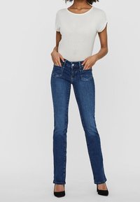 Blå denim skinny jeans med en tight passform, medelhög midja, två framfickor och minimala sömnadsdetaljer, tillsammans med en vit t-shirt med kort ärm.