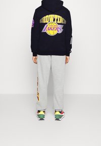 Felpa della marina con la stampa "SHOWTIME" e "LOS ANGELES LAKERS" sul retro, abbinata a pantaloni della tuta grigi con grafiche laterali, indossata con sneakers multicolore.