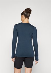 Long-sleeve top in deep blue fabric with a fitted design, smooth texture, and rounded neckline, paired with black shorts.