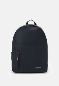 Zaino blu navy dalla forma arrotondata, realizzato in materiale testurizzato. Presenta una tasca frontale con zip e un piccolo logo nell'angolo in basso a destra.