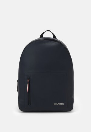 Zaino blu navy dalla forma arrotondata, realizzato in materiale testurizzato. Presenta una tasca frontale con zip e un piccolo logo nell'angolo in basso a destra.