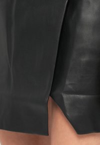 Črna usnjena krila z gladko teksturo, poševnim robom in stranskim razporkom ter prilegajočim dizajnom, ki poudari sijaj materiala.