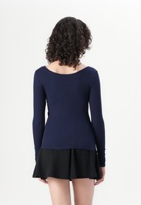 Marineblå ribbestrikket langermet topp med vid hals, tettsittende design og glatt tekstur, parret med et svart utsvingt skjørt.