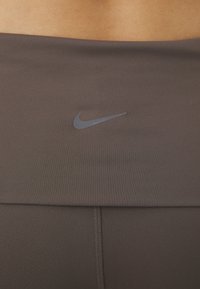 Brązowe legginsy sportowe o gładkiej teksturze. Posiadają subtelne logo Nike w ciemnoszarym kolorze na pasku oraz szwy typu flatlock zapewniające wygodę.