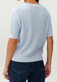 Maglione a coste blu chiaro con maniche corte, caratterizzato da un collo rotondo e una texture sottile. Indossato con jeans blu scuro.