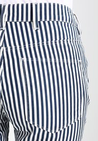 Blå och vita randiga byxor med en åtsittande midja, sidofickor och en bakficka med kontrasterande sömmar.