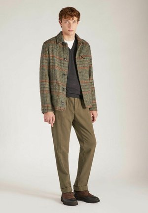 Wollmischung Jacke in Grün mit orangefarbenem Karomuster, Knopfverschluss, Brusttasche. Kombiniert mit olivfarbenen Hosen und braunen Schnürschuhen.