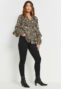 Langärmliges, knopfbares Hemd im Schlangenprint mit Schwarz- und Beigetönen; mit ausgestellten Ärmeln und lässigem Schnitt, kombiniert mit schwarzen Skinny-Jeans und Stiefeletten.